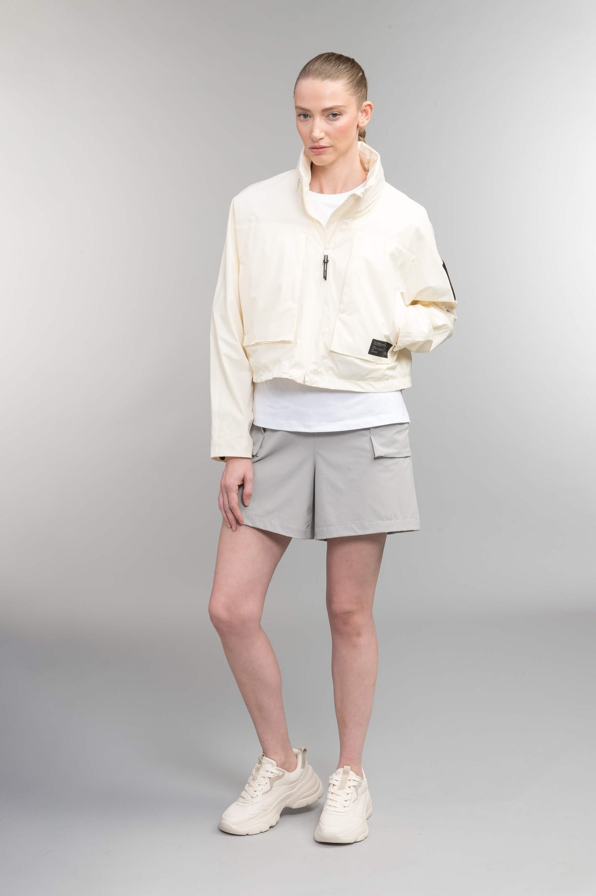 Epsie Women's Cropped Rain Jacket in Chalk crafted from premium recycled polyester ripstop with a DWR coating and taffeta nylon lining. Features a hidden packaway hood stored in the collar, two-way waterproof front zipper, seam-sealed construction, underarm zip ventilation, adjustable drawcord hem, zippered waist patch pockets, and an interior chest pocket for secure storage. Machine washable. Designed in Canada.