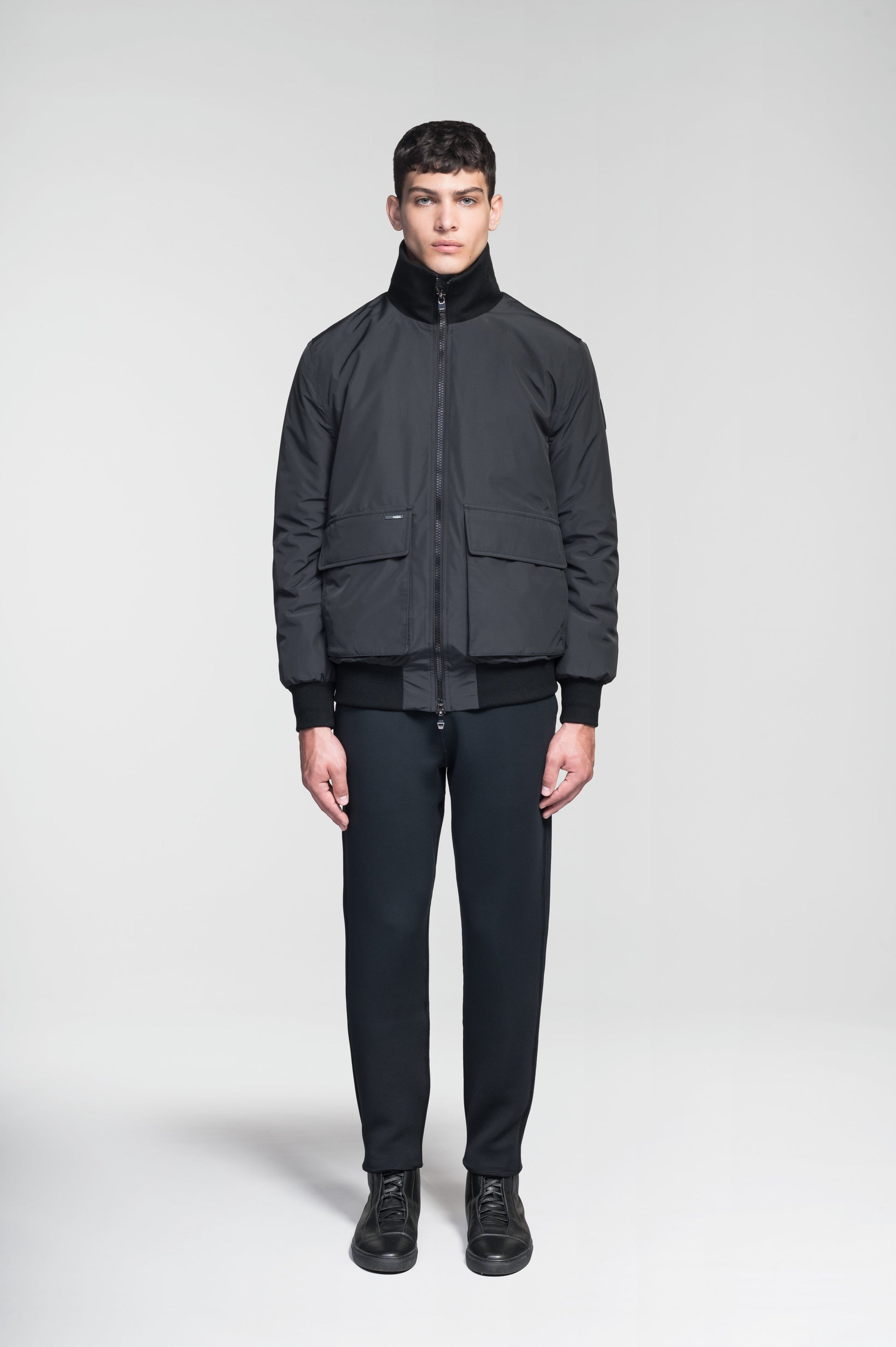 Flint Men's Tailored Rib Collar Jacket in hip length, premium 3-ply Micro Denier fabrication, premium 4-way stretch, water resistant Primaloft Gold Insulation Active +, flap pockets with magnetic closure at waist, side entry pockets at waist, ribbed sleeve cuffs, two-way branded zipper at centre front, box pleat detailing at centre back, large interior zipper pocket, and interior button pocket at left chest, in Black