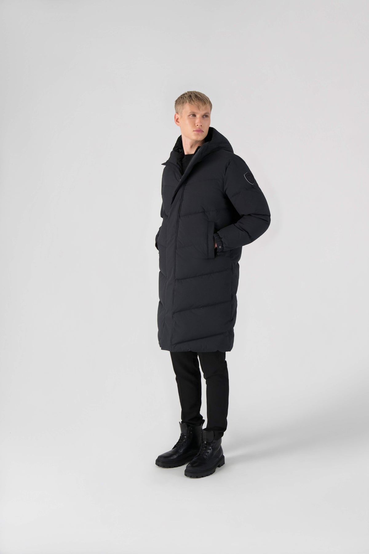 Granger long jacket in Black stretch ripstop fabric with DWR coating, insulated with Canadian white duck down and Primaloft. Features a two-way zipper, magnetic closure, and adjustable cuffs for warmth and weather protection.