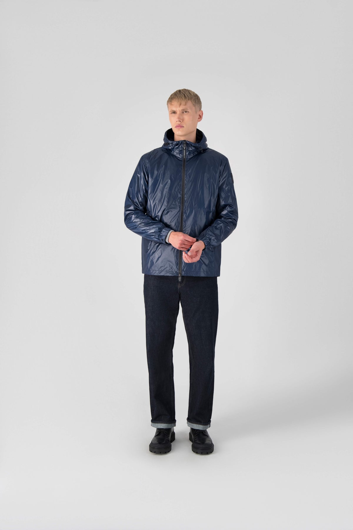 Stratus Men's Tailored Packable Rain Jacket in hip length, premium cire technical nylon taffeta and stretch ripstop fabrication, highly breathable mesh lining, hidden packable pocket, non-removable hood with adjustable draw cord, reflective piping along front and back, underarm grommets for extra breathability, back yoke with mesh ventilation, two waist zipper pockets, two interior zipper pockets, elastic cuffs with adjustable snap button, and adjustable interior draw cord at waist hem, in Marine