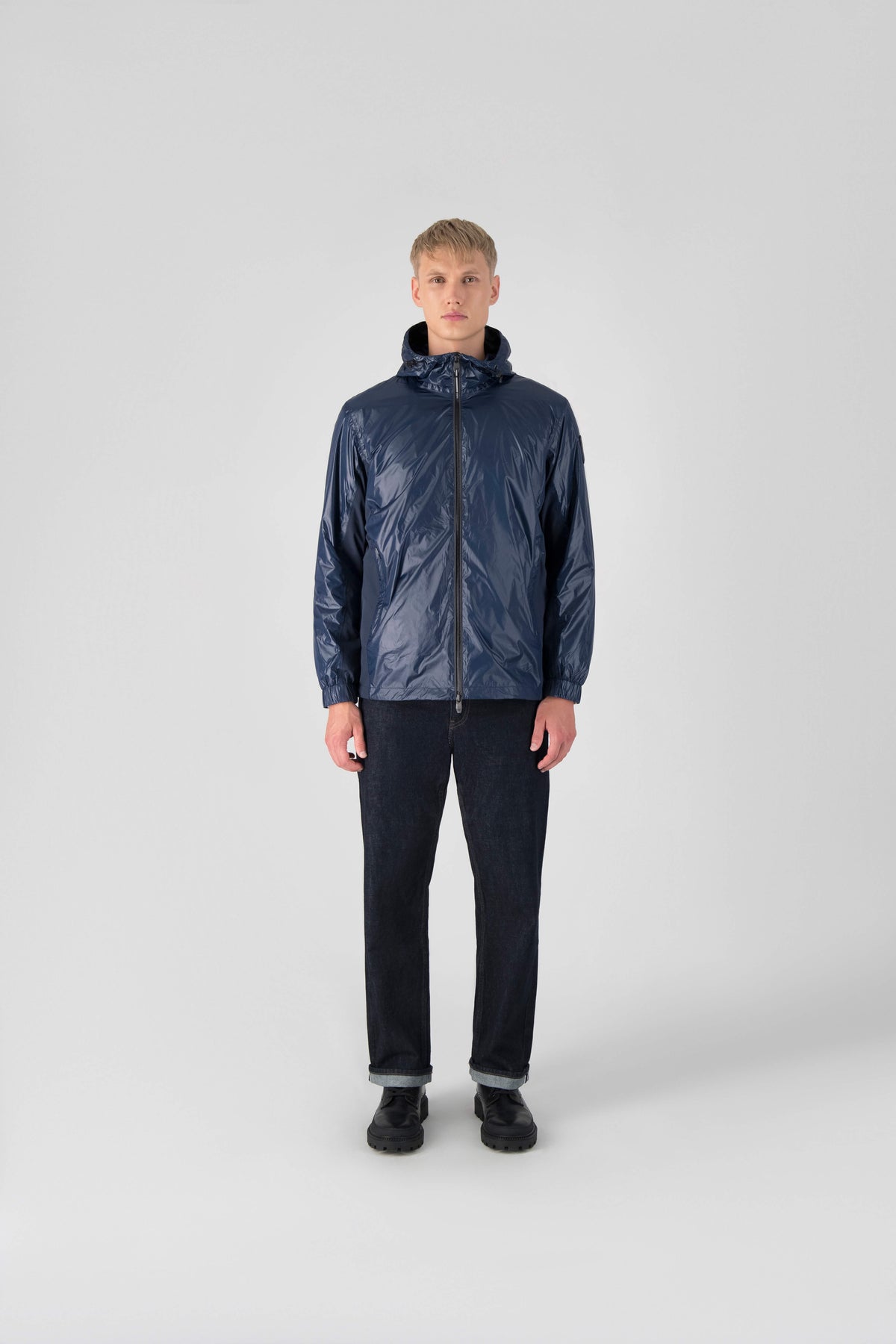 Stratus Men's Tailored Packable Rain Jacket in hip length, premium cire technical nylon taffeta and stretch ripstop fabrication, highly breathable mesh lining, hidden packable pocket, non-removable hood with adjustable draw cord, reflective piping along front and back, underarm grommets for extra breathability, back yoke with mesh ventilation, two waist zipper pockets, two interior zipper pockets, elastic cuffs with adjustable snap button, and adjustable interior draw cord at waist hem, in Marine