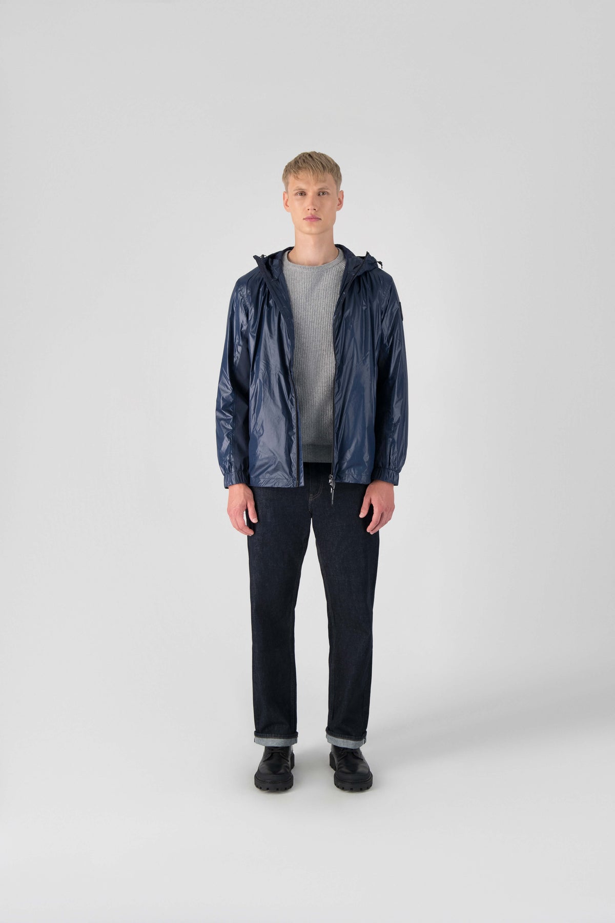 Stratus Men's Tailored Packable Rain Jacket in hip length, premium cire technical nylon taffeta and stretch ripstop fabrication, highly breathable mesh lining, hidden packable pocket, non-removable hood with adjustable draw cord, reflective piping along front and back, underarm grommets for extra breathability, back yoke with mesh ventilation, two waist zipper pockets, two interior zipper pockets, elastic cuffs with adjustable snap button, and adjustable interior draw cord at waist hem, in Marine
